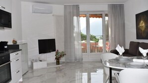 A modern living room with a flat-screen TV, a dining area with a table set for two, and a balcony with outdoor furniture. - App. 704 by Interhome (Bissone)