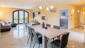 Een ruime woonkamer met een eettafel, stoelen, een bank en een groot raam.