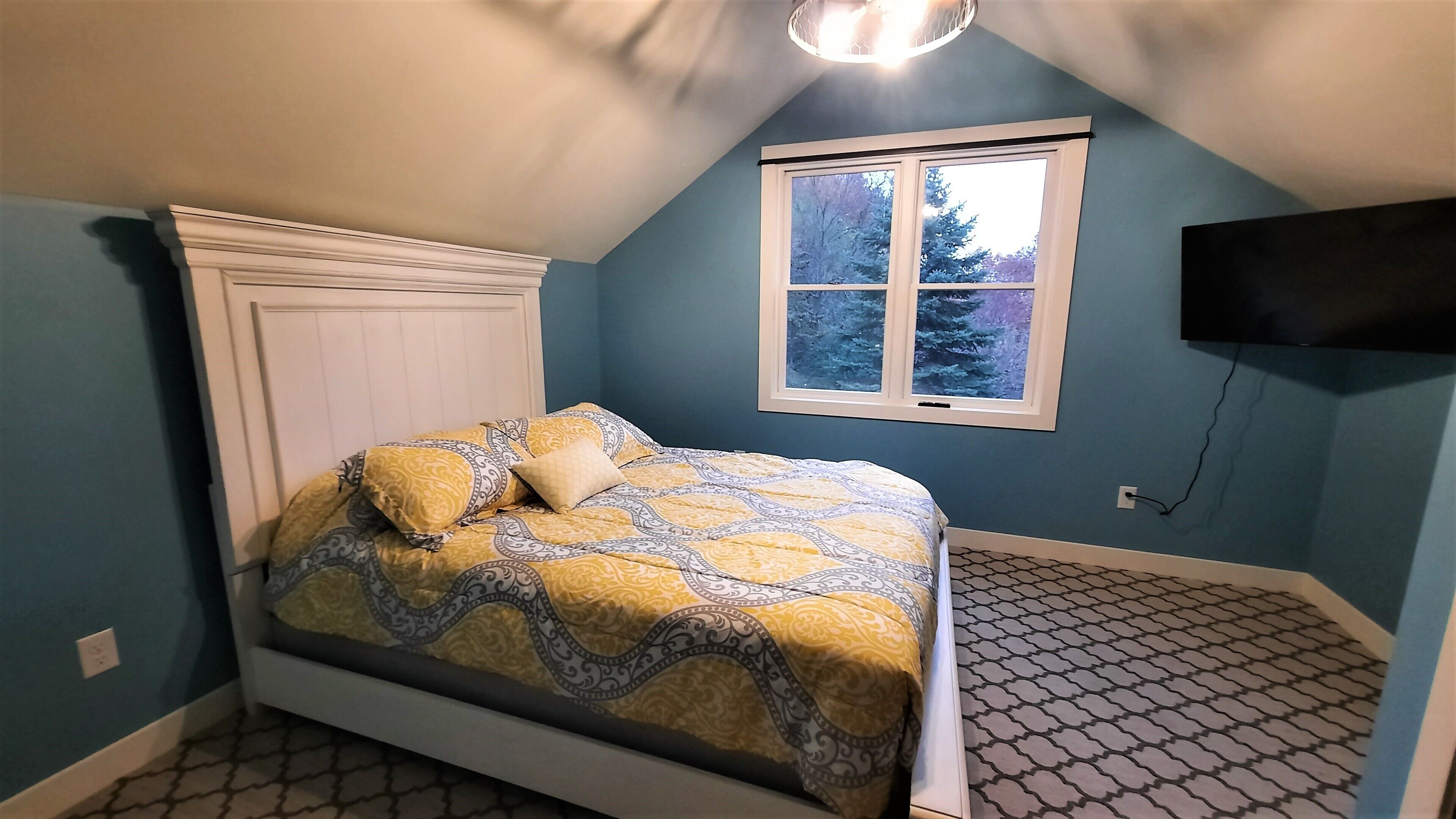 Une chambre à coucher avec un lit, une fenêtre et un téléviseur fixé au mur.