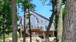 Una casa con cimientos de piedra, una terraza de madera y un árbol grande en primer plano.