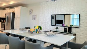 Eine moderne Küche mit weißen Schränken, einem Edelstahlkühlschrank und einem Essbereich mit weißem Tisch und grauen Stühlen.