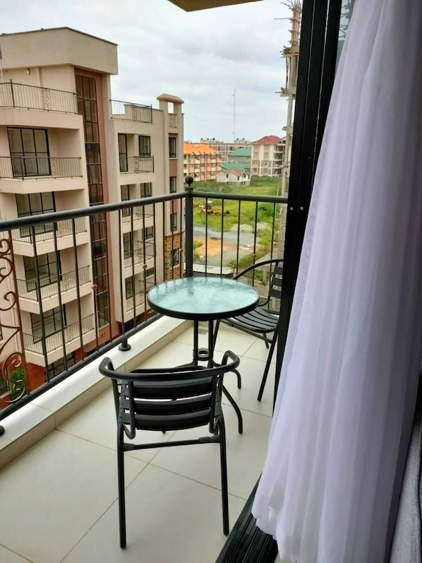 A balcony with a glass table and two chairs, overlooking a residential area with multi-story buildings.