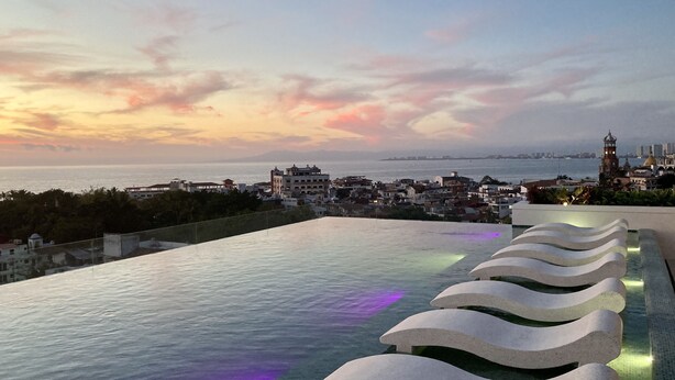 A rooftop infinity pool with a cityscape view at sunset. - Great Comfort, Location, and Style Zona Romantica (AVIDA) (Puerto Vallarta)