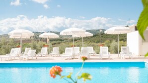 A poolside area with white lounge chairs and umbrellas, a clear blue pool, and a view of green hills in the background. - Apartment in the Gargano Park (Vieste (FG))