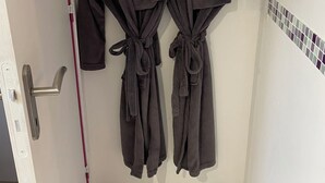 Dos túnicas oscuras colgadas en un perchero en un baño con suelo de baldosas y una puerta con pomo rojo.