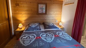 Une chambre avec des murs recouverts de lambris en bois, un lit avec une literie à motifs, deux lampes de chevet et un tableau encadré au mur.