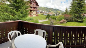 Un balcon avec une table ronde et des chaises, donnant sur une région montagneuse parsemée de bâtiments et de verdure.