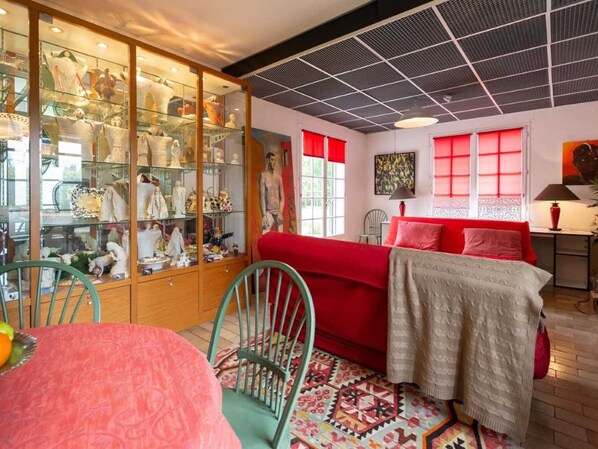 A room with a red sofa, a glass display cabinet with various items, and a patterned rug.