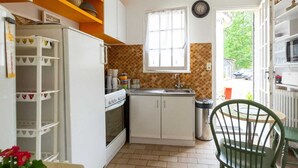 Uma cozinha compacta com armários brancos, um fogão e uma pia. Há uma janela acima da pia, e uma cadeira é visível em primeiro plano.