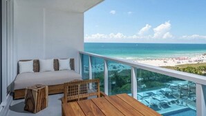 Ein Balkon mit einem Bett, einem Holztisch und Blick auf Strand und Meer.