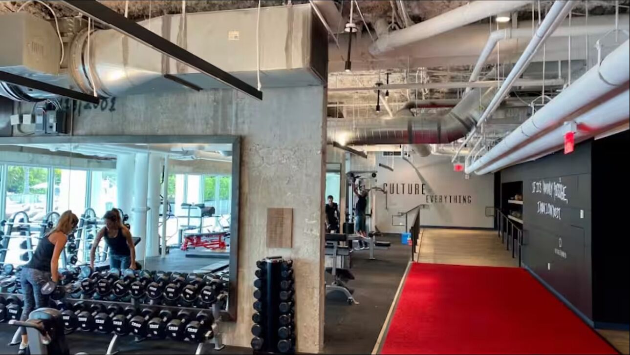 Et fitnesscenter med vægtstativer, træningsudstyr og et rødt løbende tæppe.