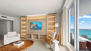 Ein modernes Wohnzimmer mit einem Flachbildfernseher, weißen Sofas, einem Holztisch und einem Korbstuhl.