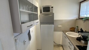 A compact kitchen with a built-in microwave, a refrigerator, a sink, and a countertop with a kettle and a pot. - Apartment Harzblick -neu Modernisiert- (Sankt Andreasberg)