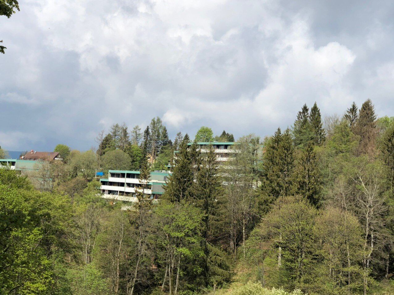 A multi-story building surrounded by dense forest with a cloudy sky.
