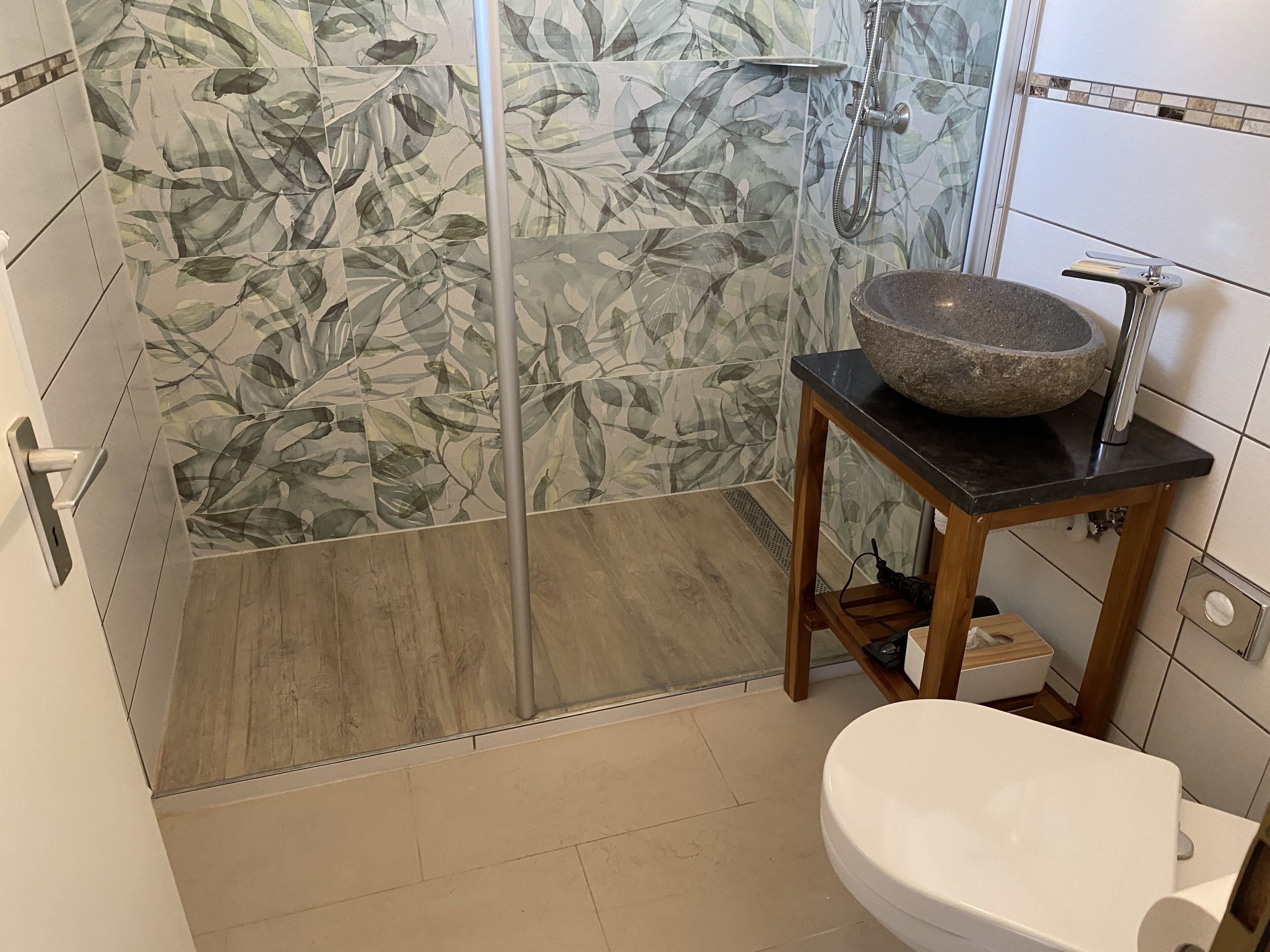 Een badkamer met een douche, een stenen wastafel op een houten standaard en een toilet.