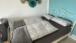 A bed with a dark mattress, grey and white patterned pillows, a grey throw blanket, and a white metal headboard. - Apartment Harzblick -neu Modernisiert- (Sankt Andreasberg)