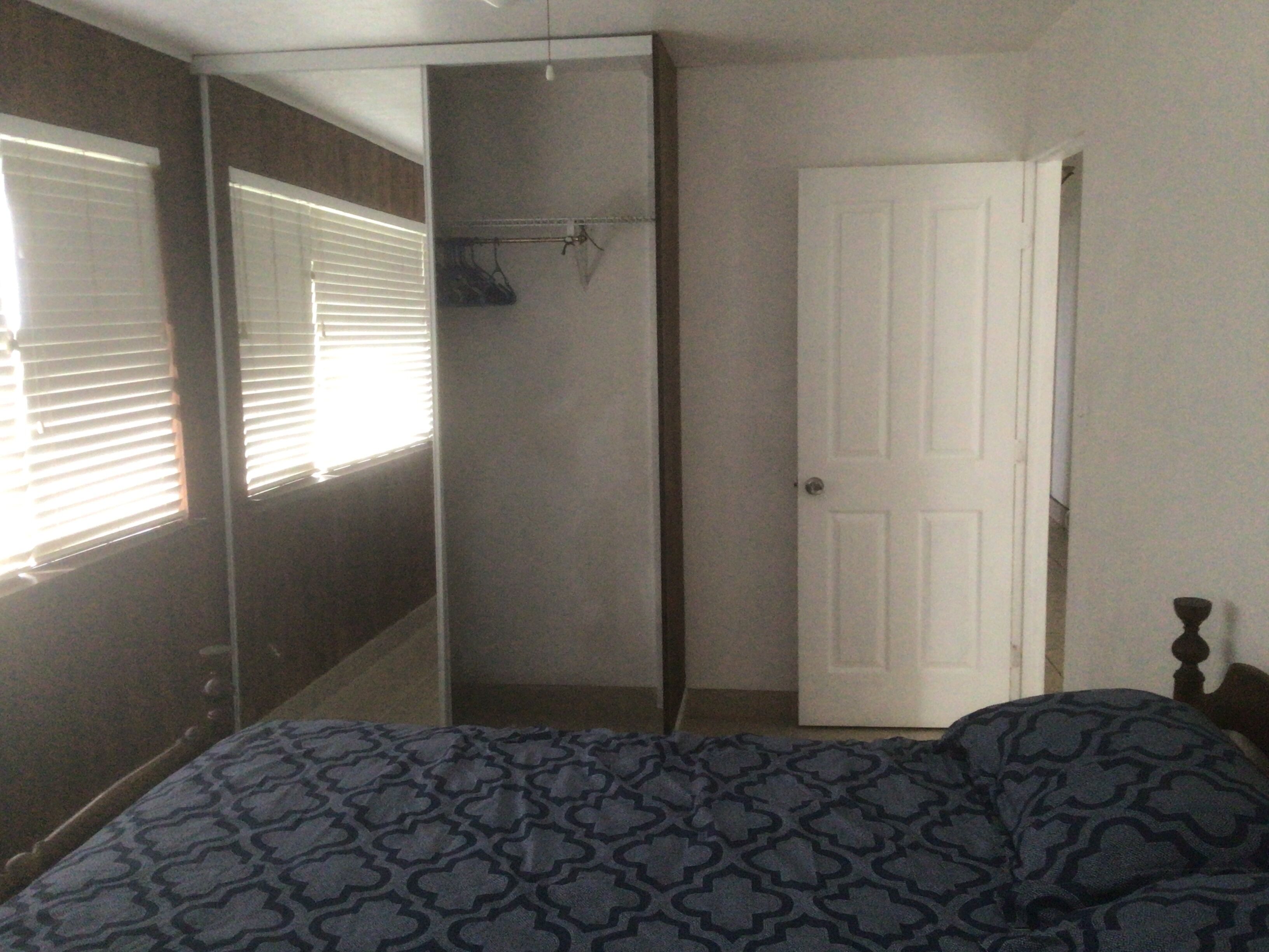 Un dormitorio con cama, armario, puerta y ventana con persianas.
