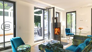 A modern living room with a glass fireplace, blue furniture, and large windows. - Beach Cloud Luxury Apartment: Private Sauna, Pool, and Beach Chair | Terrace | Fireplace (Binz)