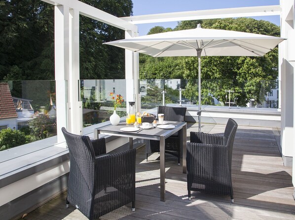 A modern outdoor dining area with a table, chairs, and an umbrella. - Beach Cloud Luxury Apartment: Private Sauna, Pool, and Beach Chair | Terrace | Fireplace (Binz)