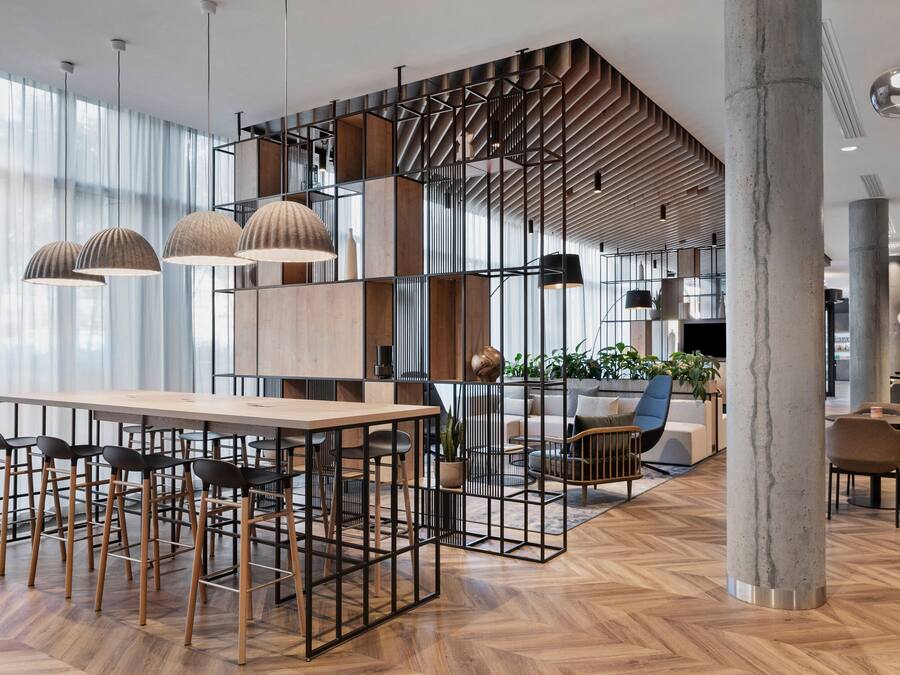 Ein modernes Interieur mit Holzdielen im Fischgrätmuster, einer zentralen Bar mit Hockern und einer Sitzecke mit Sofas und Sesseln.
