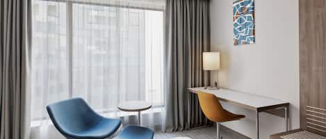 Quarto de hotel com cama, escrivaninha, cadeira e uma mesinha.