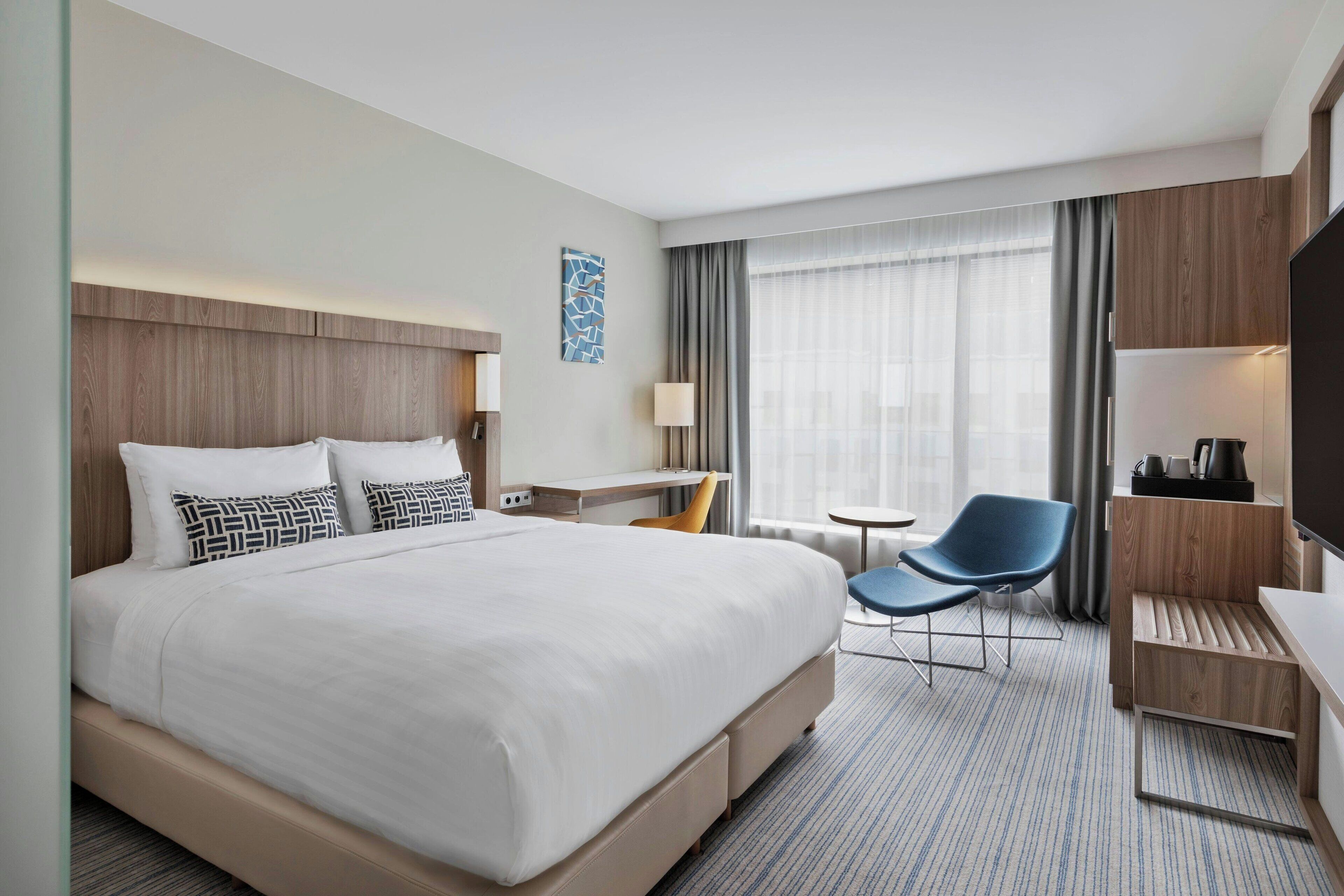A hotel room with a large bed, a desk, a chair, and a TV.