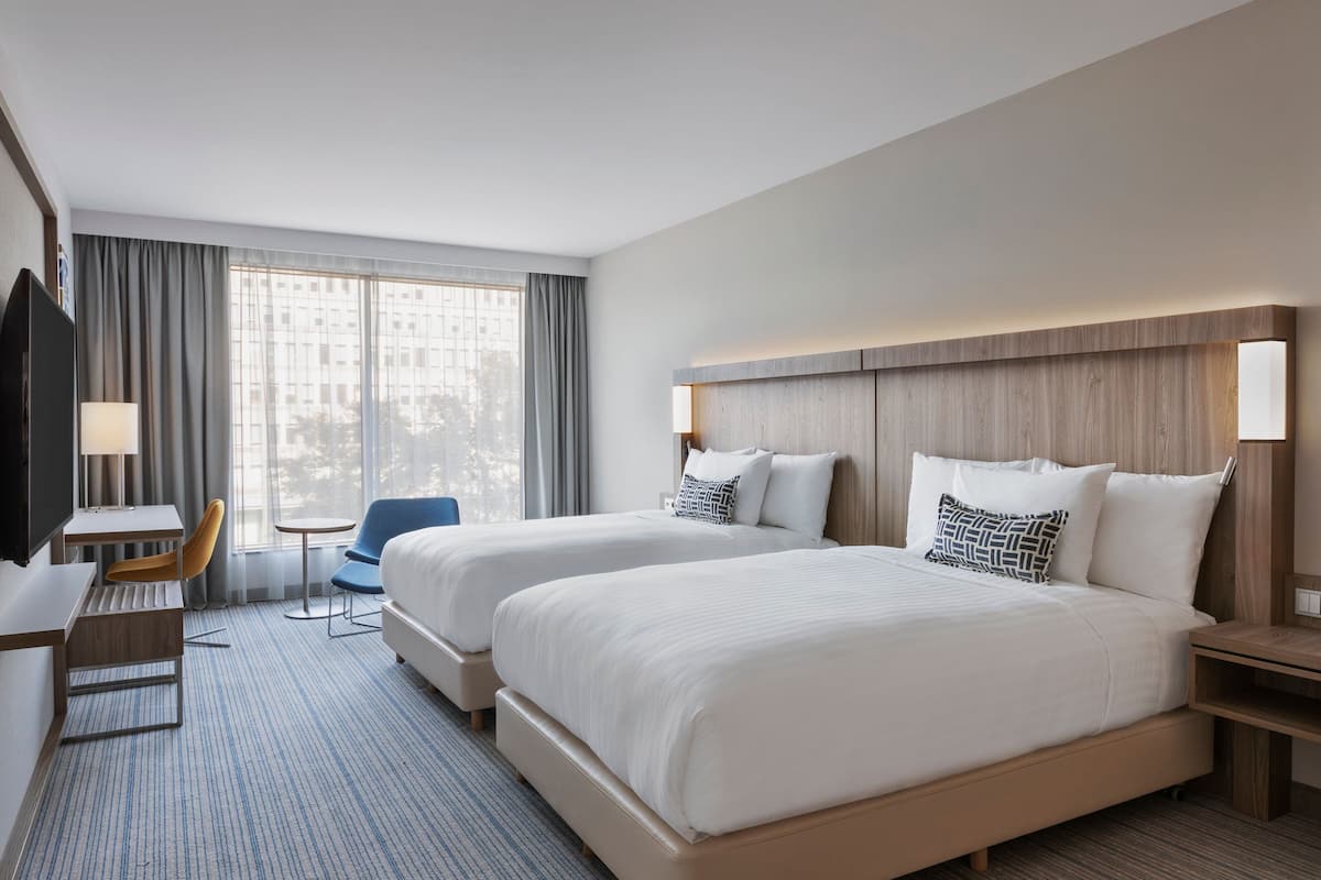 Une chambre d’hôtel avec deux lits, un bureau, une chaise et un téléviseur.