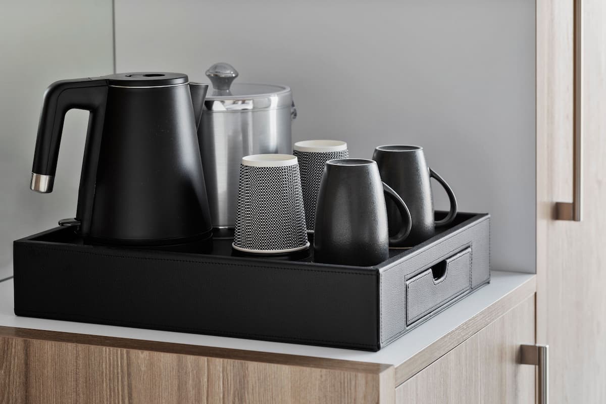 Une machine à café noire, une casserole en acier inoxydable et plusieurs tasses noires sur un comptoir blanc.