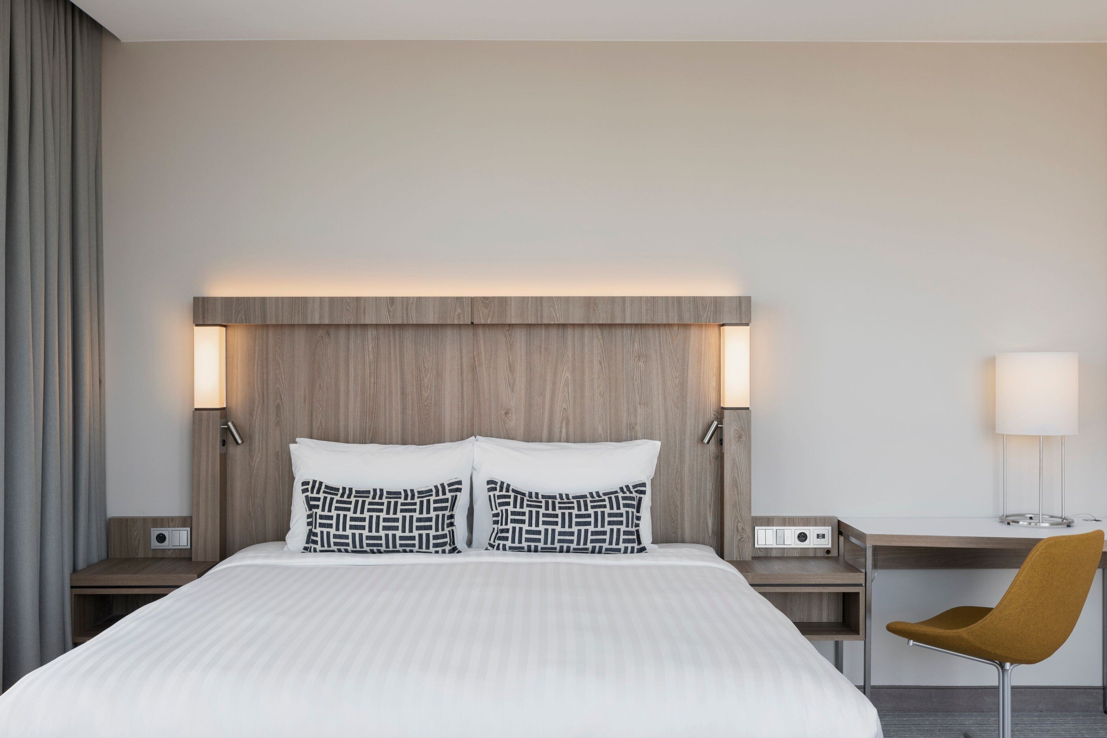 A modern hotel room with a large bed, two bedside tables, a desk, and a chair.