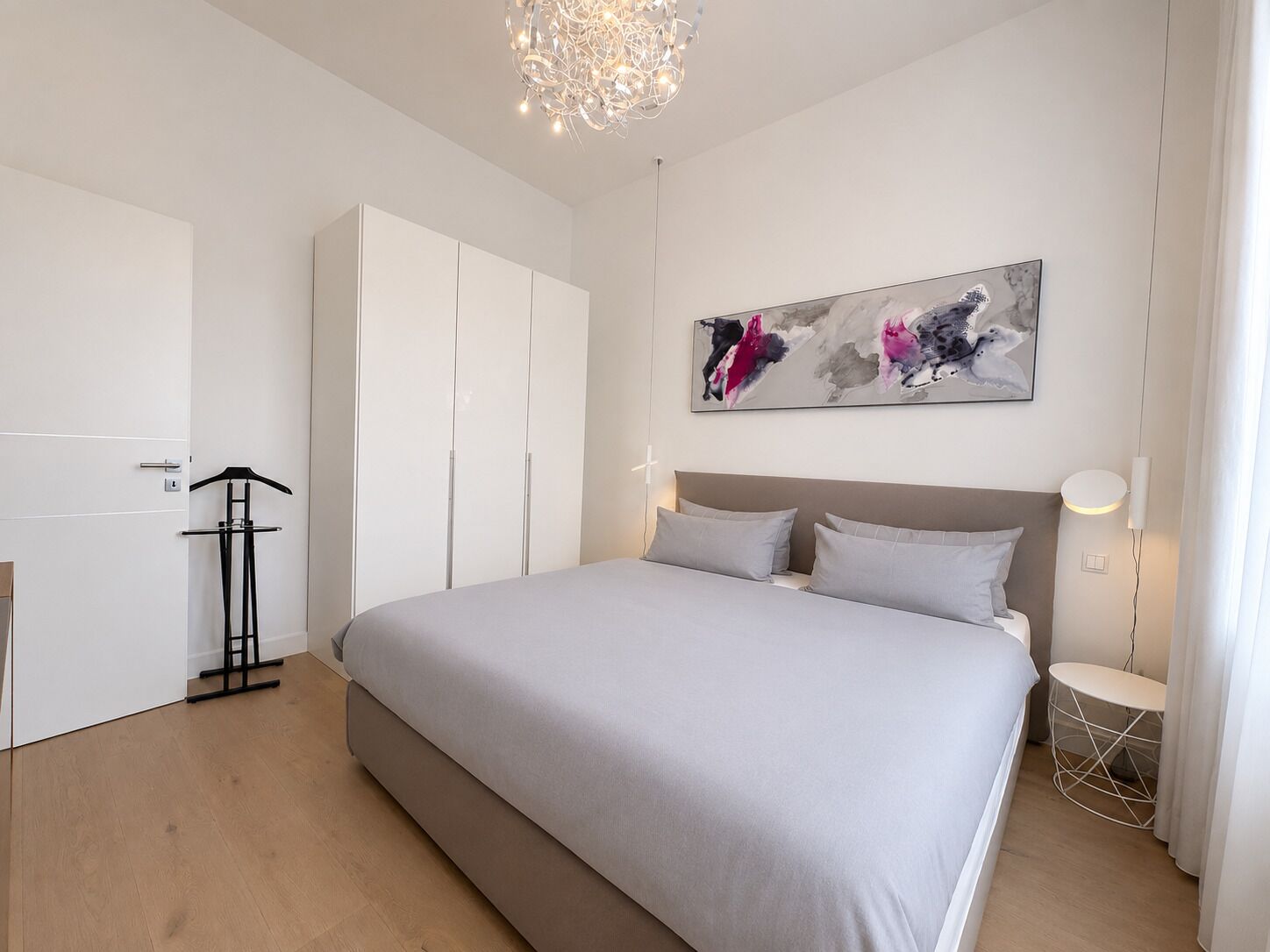 Une chambre à coucher moderne avec un grand lit, une armoire, un porte-manteau et un tableau abstrait accroché au mur.