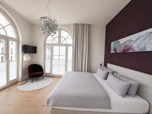 Ein modernes Schlafzimmer mit einem großen Bett, einem runden Teppich, einem Sessel, einem Fernseher und einem Gemälde an der Wand.