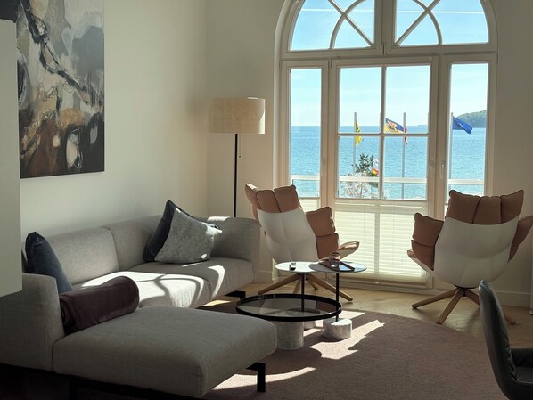 Un salon comprenant un canapé, des fauteuils, une table basse et offrant une vue sur la mer grâce à de grandes fenêtres.