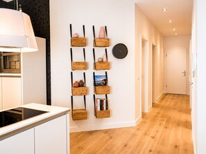 A modern kitchen with white cabinets and a wooden countertop, a hallway with wooden flooring, and a wall-mounted clock. - House (Binz)