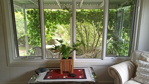 A room with a large window overlooking a garden, a small table with a plant, and a sofa.