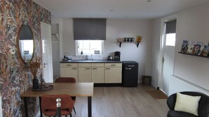A modern kitchen with a dining area, featuring a wooden table, chairs, and a black refrigerator. - Beautiful b&b/ vacation home located on a large garden surrounded by water. (Bovenkarspel)