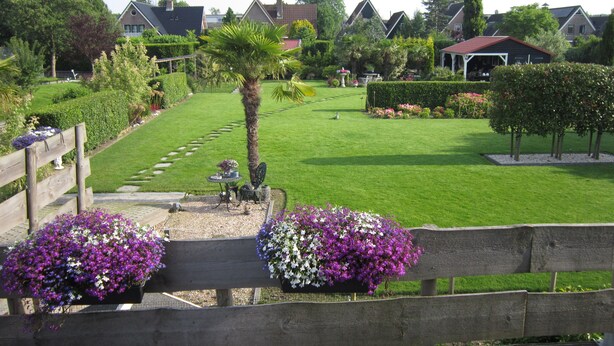 A well-maintained garden with a wooden bench, a small table, and a variety of flowers. - Beautiful b&b/ vacation home located on a large garden surrounded by water. (Bovenkarspel)