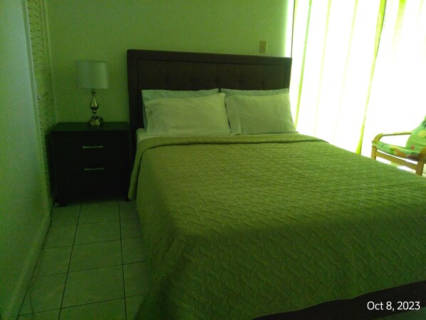 A hotel room with a bed, a nightstand with a lamp, and a chair. - Mobay Club Irresistible View (Montego Bay)