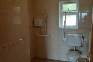 A small bathroom with a toilet, a shower, and a window.