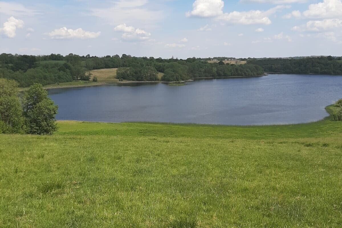 A large, calm lake surrounded by lush green fields and trees.