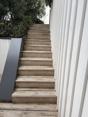 A wooden staircase leading up to a white building, surrounded by greenery.