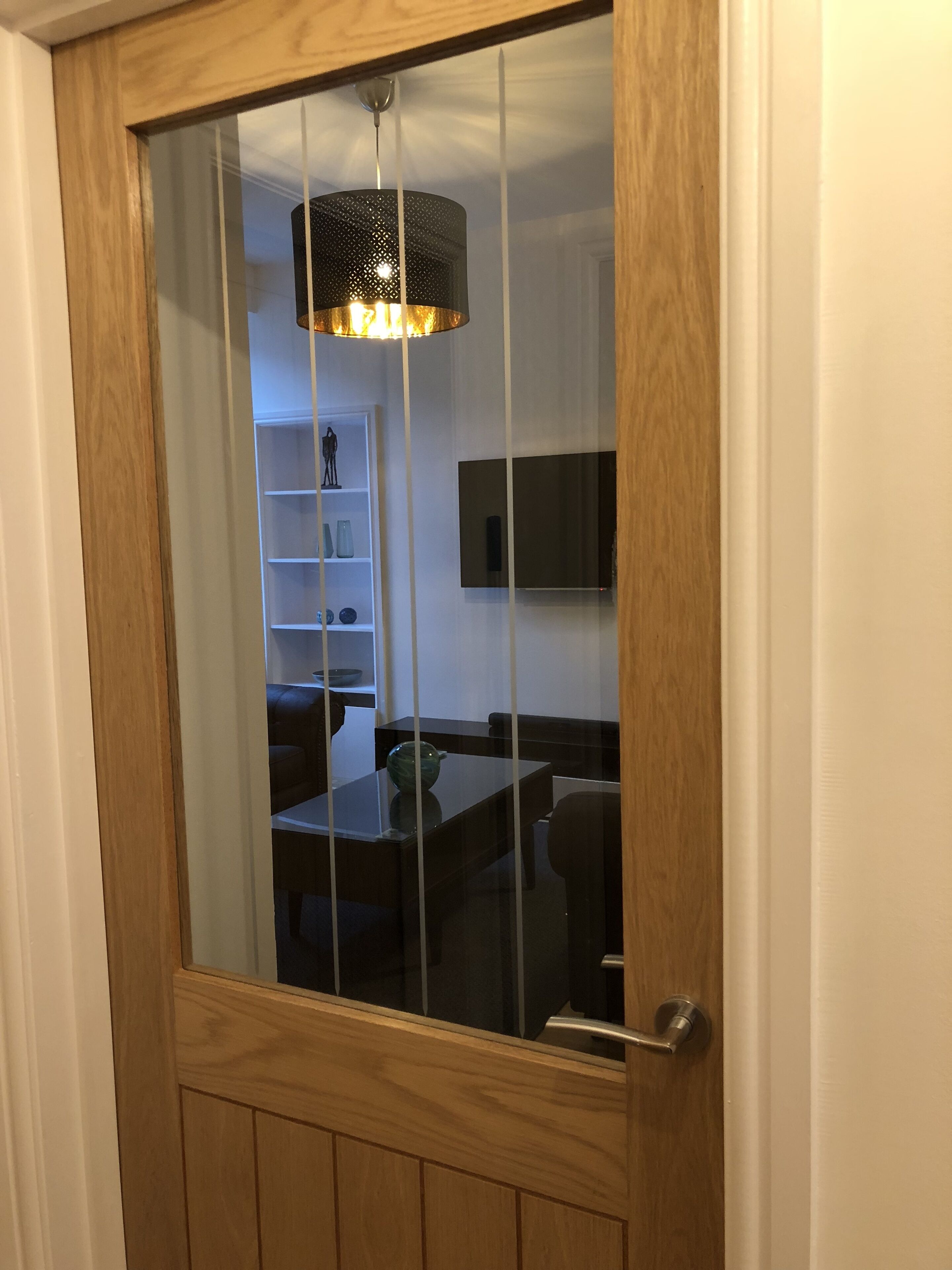 A wooden-framed door with a glass panel, leading to a room with a dining table, chairs, a TV, and a shelf with decorative items.