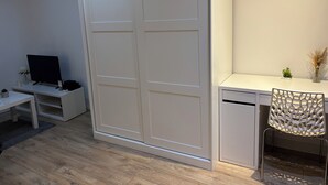Una habitación moderna con un armario corredero, un escritorio con silla, televisor y una planta pequeña.