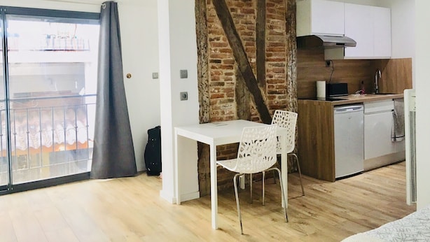 Una cocina moderna con pared de ladrillo decorativa, una mesa de comedor blanca con una silla blanca y un amplio ventanal corredizo que da a un balcón.
