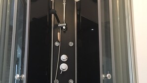 Un box de ducha con paredes de vidrio, una ducha de mano y un panel de control montado en la pared.
