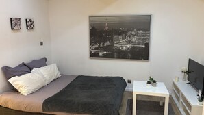 Un dormitorio moderno con una cama, una mesita de noche, un televisor y un cuadro con una vista urbana en la pared.