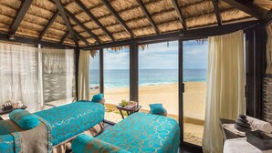 A room with two beds, a view of the beach, and a thatched roof.