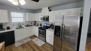 Une cuisine moderne avec des meubles blancs, des appareils en acier inoxydable, un ventilateur de plafond et une fenêtre équipée de stores.