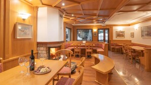 A cozy restaurant with wooden interiors, a fireplace, and multiple seating areas including booths and tables. - Hotel Posta (Aprica)