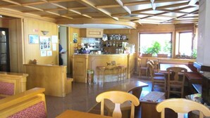 A restaurant with wooden furniture, a bar area, and a kitchen in the background. - Hotel Posta (Aprica)