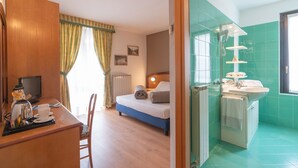 A hotel room with a bed, a desk with a computer, a chair, a window with curtains, a radiator, and a bathroom with a sink and mirror. - Hotel Posta (Aprica)